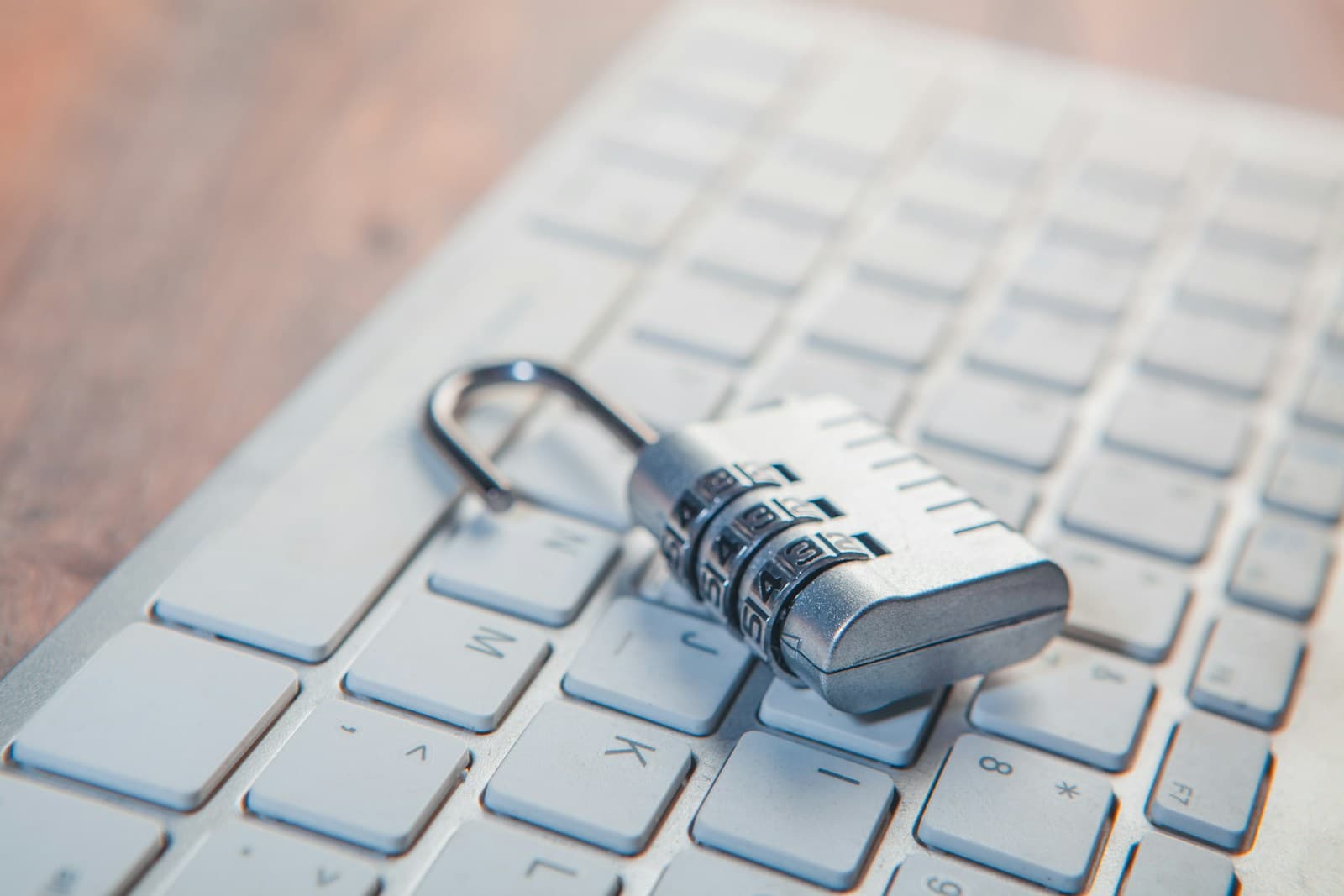 Cadeado de combinação aberto pousado sobre um teclado branco.